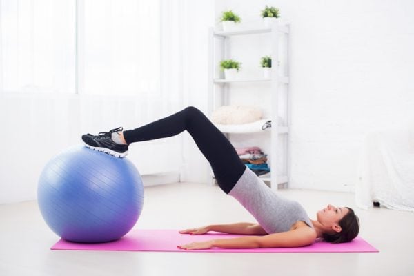 sporty woman doing pilates exercise lifting her pelvis with fit ball at home.